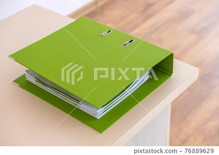 Green binder with office documents on a working table. Green binder with office documents on a working table. 76889629