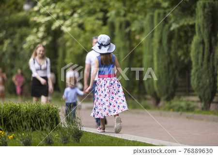 Little child girl in summer dress and a hat walking alone in green park. Little child girl in summer dress and a hat walking alone in green park. 76889630