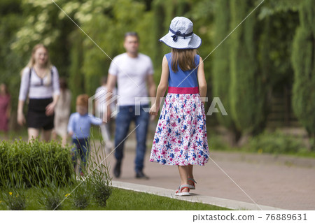 Little child girl in summer dress and a hat walking alone in green park. Little child girl in summer dress and a hat walking alone in green park. 76889631