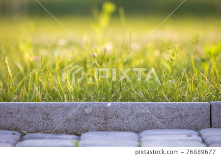 Closeup of pavement curb with green grass lawn behind. Closeup of pavement curb with green grass lawn behind. 76889677