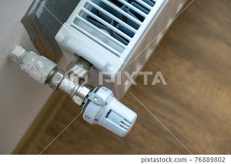 Closeup of heating radiator valve for comfortable temperature regulation on metal radiator on inrerior wall. Closeup of heating radiator valve for comfortable temperature regulation on metal radiator on inrerior wall. 76889802