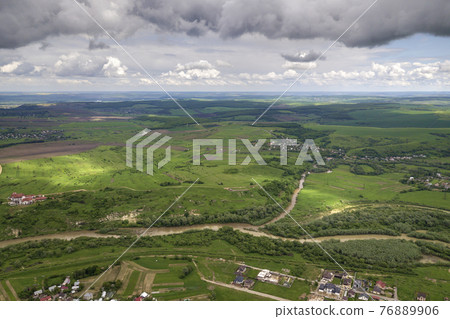 Aerial view of town or village with rows of buildings and curvy streets between green fields in summer. Countryside landscape from above. Aerial view of town or village with rows of buildings and curvy streets between green fields in summer. Countryside landscape from above. 76889906