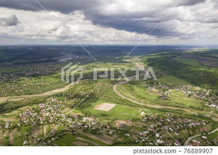 Aerial view of town or village with rows of buildings and curvy streets between green fields in summer. Countryside landscape from above. 76889907