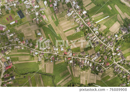 Top down aerial view of town or village with rows of buildings and curvy streets between green fields in summer. Countryside landscape from above. Top down aerial view of town or village with rows of buildings and curvy streets between green fields in summer. Countryside landscape from above. 76889908