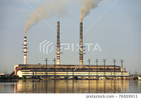 Thermal power station tall pipes with thick smoke reflected in lke water surface. Pollution of environment concept. Thermal power station tall pipes with thick smoke reflected in lke water surface. Pollution of environment concept. 76889911