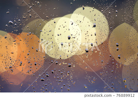 Abstract colorful bokeh background with yellow circles and water drops on glass surface in front. Blurred city lights. Abstract colorful bokeh background with yellow circles and water drops on glass surface in front. Blurred city lights. 76889912