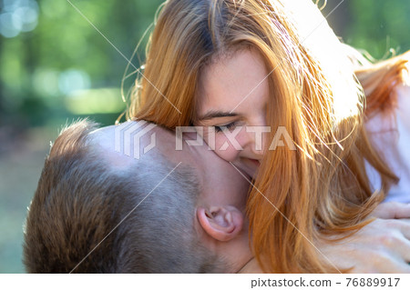 Beautiful teenage girl with bright red hair hugging her boyfriend outdoors. First love and romantic relationship concept. Beautiful teenage girl with bright red hair hugging her boyfriend outdoors. First love and romantic relationship concept. 76889917