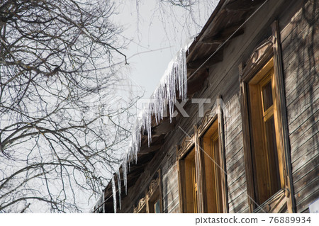 Icicles hang from the roof of a wooden house and shine in the sun.  76889934