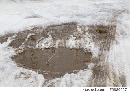 Car wheel and tire tracks on a small puddle of melted snow. Car wheel and tire tracks on a small puddle of melted snow. 76889937