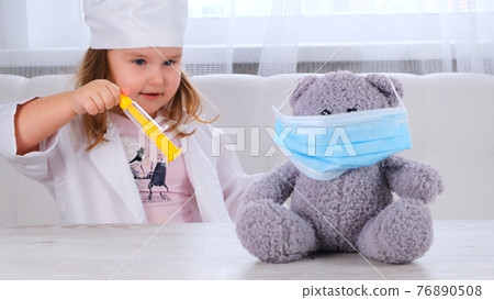little girl plays a doctor, makes an injection. Happy child little doctor examines a teddy bear little girl plays a doctor, makes an injection. Happy child little doctor examines a teddy bear 76890508