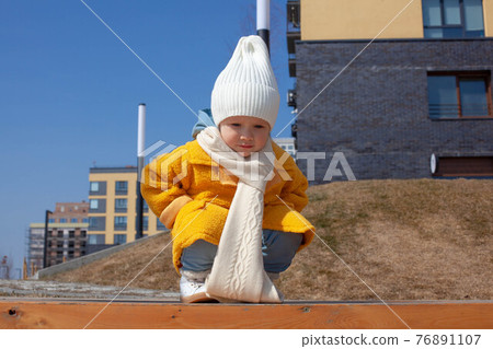 Beautiful baby in an orange coat and white hat and scarf Beautiful baby in an orange coat and white hat and scarf 76891107