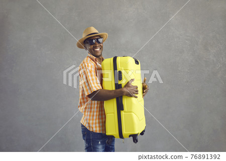 Studio portrait of happy smiling black tourist holding his yellow travel suitcase Studio portrait of happy smiling black tourist holding his yellow travel suitcase 76891392