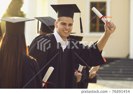 Smiling happy university graduate holding diploma in raised hand Smiling happy university graduate holding diploma in raised hand 76891454