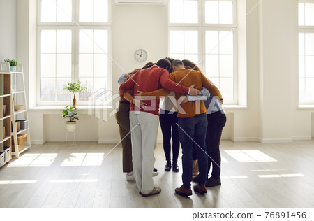 Group of diverse friends or colleagues huddling standing together in a modern light office Group of diverse friends or colleagues huddling standing together in a modern light office 76891456