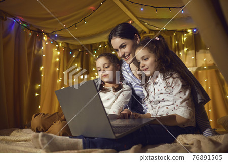 Mother and two daughter children watching funny cartoon on laptop before bedtime 76891505