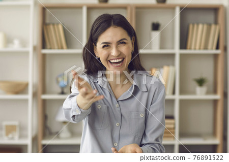 Webcam portrait of cheerful young woman holding out hand encouraging you to speak Webcam portrait of cheerful young woman holding out hand encouraging you to speak 76891522