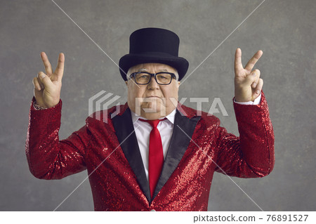 Portrait of funny serious rich senior man in top hat and sequin jacket showing V sign 76891527
