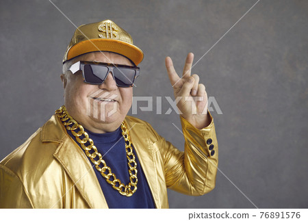 Funny and cheerful senior man in luxury clothes showing v-sign on gray background. 76891576