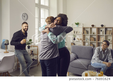Two excited young people hug each other as they meet at a friends' reunion party Two excited young people hug each other as they meet at a friends' reunion party 76891624