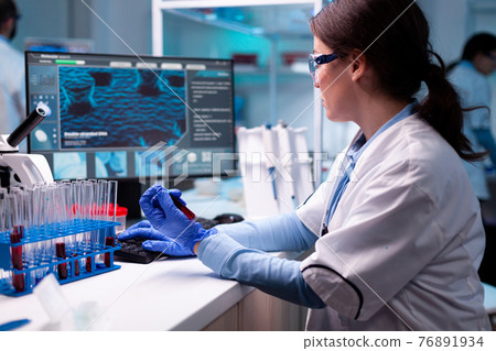 Scientist typing on laptop holding vacutainer blood healthcare chemistry 76891934