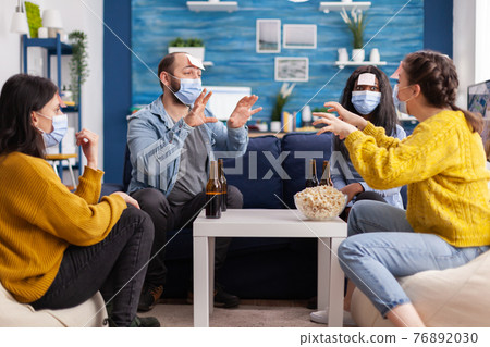 Happy cheerful multi ethnic friends with face mask playing game 76892030