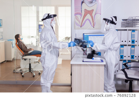 Dental receptionist dressed in coverall giving doctor patient x-ray 76892128