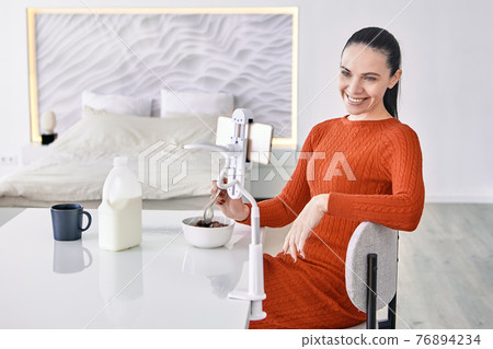 An adult woman uses phone holder at dining table. An adult woman uses phone holder at dining table. 76894234
