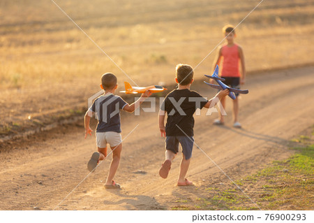 children have fun outdoors, three boys in nature, run and play with toy airplanes, the concept of childhood 76900293