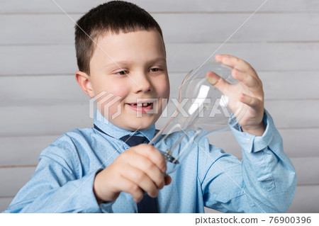 cheerful boy holds a light bulb in two hands and examines it, the concept of learning 76900396