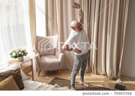 Senior bald man in yoga side stretch asana doing exercies alone at home. 76903568