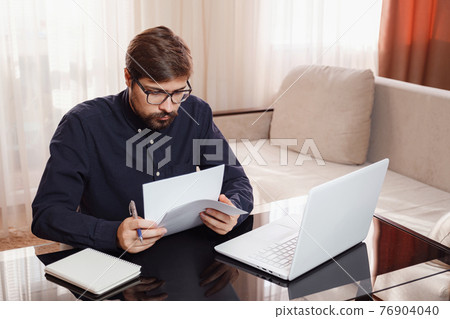 Entrepreneur works with a laptop and keeps a document in a home office Entrepreneur works with a laptop and keeps a document in a home office 76904040