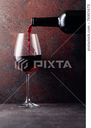 Red wine is poured from a bottle into a wine glass on rusty brown background. Red wine is poured from a bottle into a wine glass on rusty brown background. 76905678