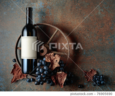 Bottle of red wine with grapes and dried vine leaves on an old rusty background. 76905690