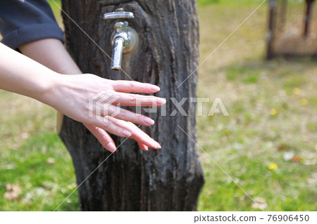 A woman washing her hands during a walk in a park on a warm spring day 76906450