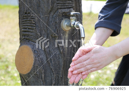 A woman washing her hands during a walk in a park on a warm spring day 76906925