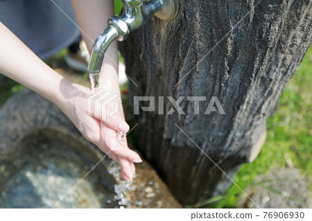 A woman washing her hands during a walk in a park on a warm spring day 76906930