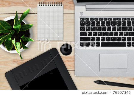 Wooden desk with laptop, notepad with blank sheet, pot of flower, stylus and tablet for retouching. Workspace of professional retoucher. Creativity, design, art and modern equipments concept Wooden desk with laptop, notepad with blank sheet, pot of flower, stylus and tablet for retouching. Workspace of professional retoucher. Creativity, design, art and modern equipments concept 76907345