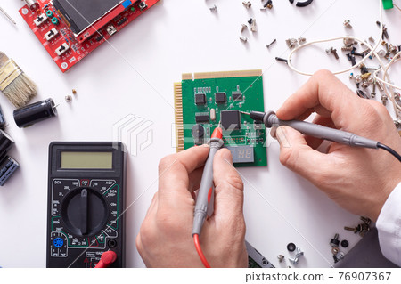 Close up of hands of man repairing computer part with soldering iron, repairman working, faceless shot of repair computer wizard soldering motherboard at table surrounded different nuts and devices. 76907367