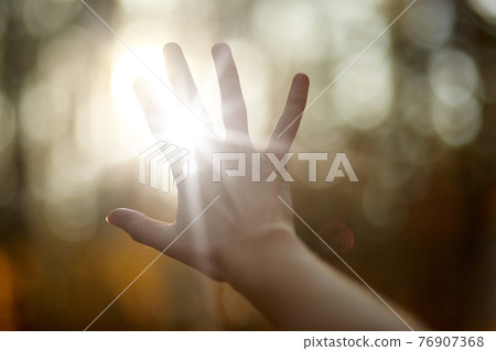 Faceless picture, man's hand covering sunlight,l sun shiing through hand, image of human's hand covering sun, bright rays of sun, isolated over park or forest background. Nature concept. 76907368