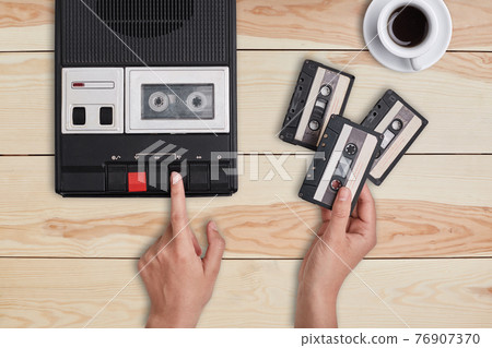 Retro stuff, old items, memories. Hands switching on old tape cassette recorder and holding three cassettes choosing which song to reproduce. Woman listening to old songs remebering her youth Retro stuff, old items, memories. Hands switching on old tape cassette recorder and holding three cassettes choosing which song to reproduce. Woman listening to old songs remebering her youth 76907370