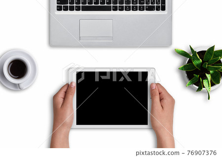 Woman`s hands holding modern tablet with blank screen over white background. Modern devices: tablet and laptop computer on white surface with cup of coffee and flowerpot with flower. Office design Woman`s hands holding modern tablet with blank screen over white background. Modern devices: tablet and laptop computer on white surface with cup of coffee and flowerpot with flower. Office design 76907376