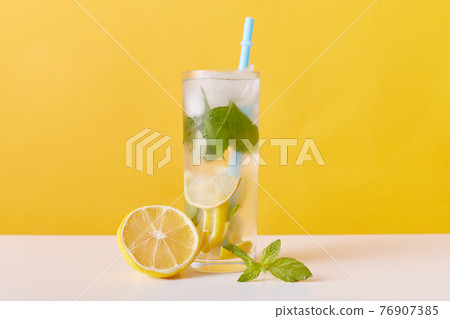 Homemade refreshing summer lemonade drink with lemon slices, mint and ice cubes, glasses with drinking straw isolated over yellow wall, detox cocktail. Homemade refreshing summer lemonade drink with lemon slices, mint and ice cubes, glasses with drinking straw isolated over yellow wall, detox cocktail. 76907385