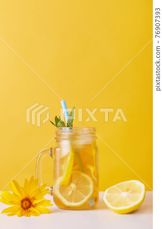 Glass of lemonade with lemon and mint, drinking straw in glass cup isolated over yellow background, fresh lemonade or cold tea. Copy space for advertisement. Glass of lemonade with lemon and mint, drinking straw in glass cup isolated over yellow background, fresh lemonade or cold tea. Copy space for advertisement. 76907393