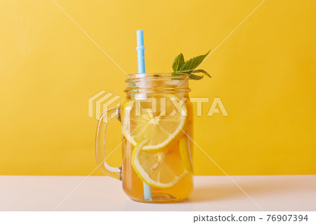 Close up shot of fresh drink with lemons and mint, glass jug filled with cocktail and lemon slices and drinking tube, cold summer refreshing lemonade. Close up shot of fresh drink with lemons and mint, glass jug filled with cocktail and lemon slices and drinking tube, cold summer refreshing lemonade. 76907394