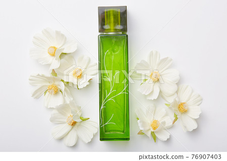 Perfume for women in green bottle and flowers around isolated over white background. Pleasant aromat or odor. Floral fragrance 76907403