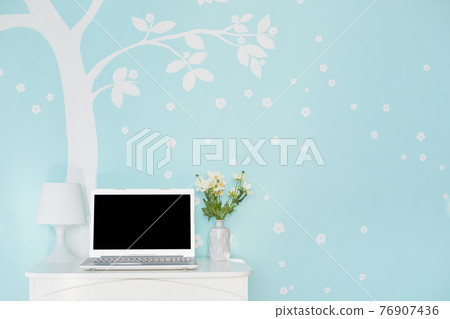 Shot of modern laptop computer with blank screen for your text on white table, lamp and flowers against light blue wall decorated with white tree print. Technology and furniture concept 76907436