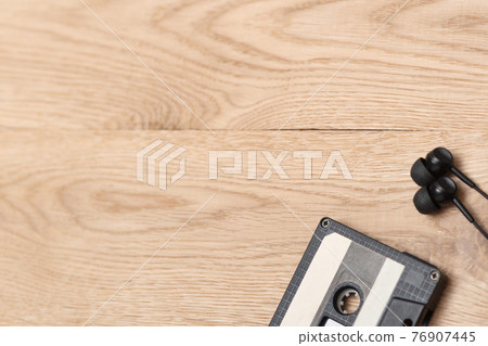 Shot of audio cassette and earphones in right corner over wooden surface. Music and revolution. Musical objects. Selective focus. Vintage style Shot of audio cassette and earphones in right corner over wooden surface. Music and revolution. Musical objects. Selective focus. Vintage style 76907445