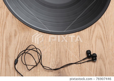 Vinyl record and contemporary earphones on wooden flat background. Music and revolution concept. Top view. Vinyl record and contemporary earphones on wooden flat background. Music and revolution concept. Top view. 76907446