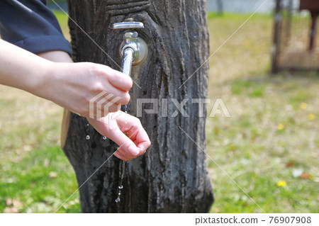 A woman washing her hands during a walk in a park on a warm spring day 76907908