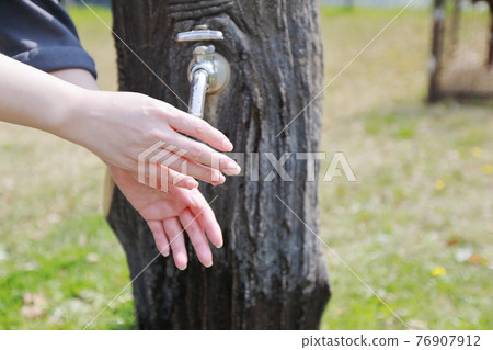 A woman washing her hands during a walk in a park on a warm spring day 76907912